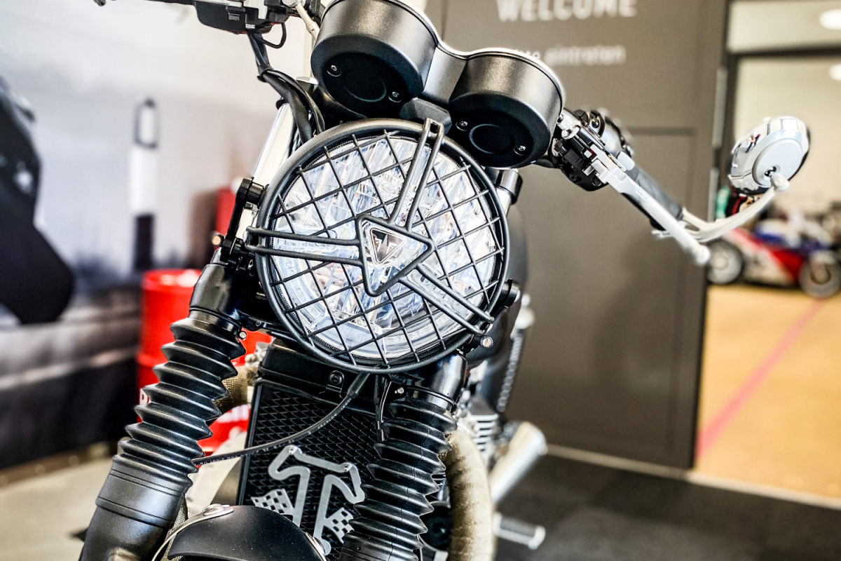 Triumph Thruxton Schwarz mit Frontleuchte und Triumph Logo vor Showroom – Customizing Motorrad